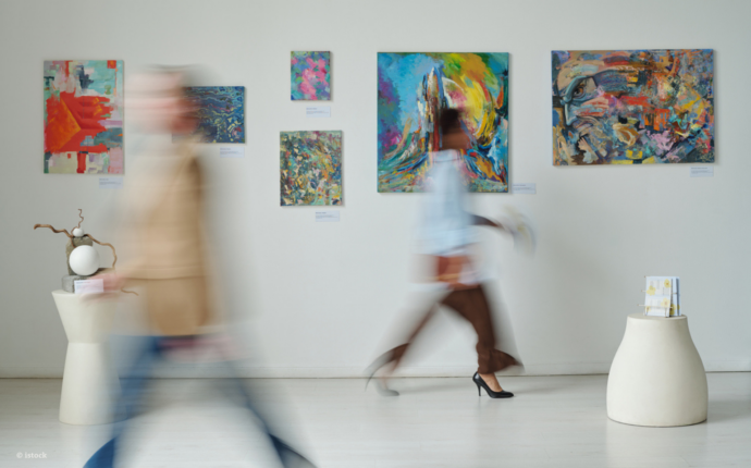 A scene from an art gallery. The walls are white, and brightly coloured abstract art is on the wall. 