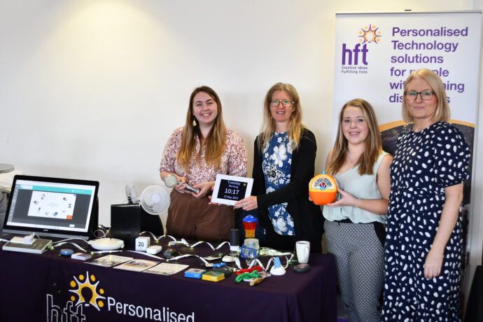 This is a picture of colleagues from Hft, stood in front of a Hft banner that says 'personalised technology solutions for people with learning disabilities.' 